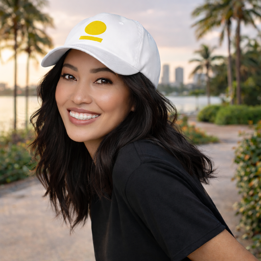 Woman wearing a white STOIC cap with embroidered logo in an outdoor setting with palm trees and water.