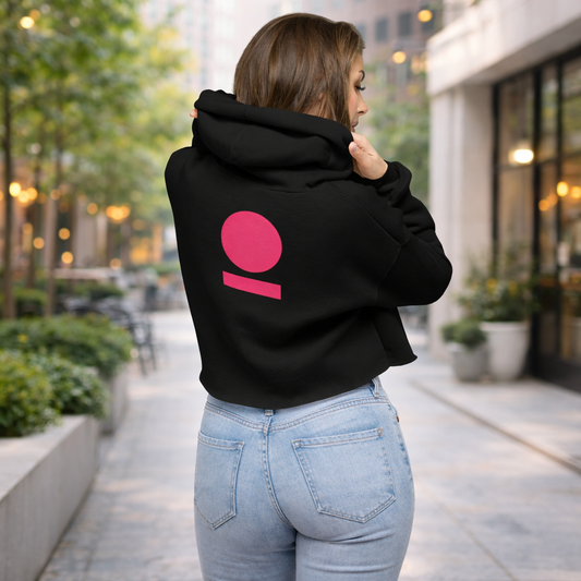 Person wearing a black hoodie with a pink logo on the back, standing on a city street.