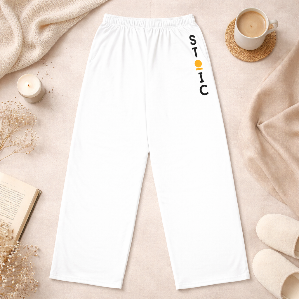 Back of white STOIC pants with vertical logo on a beige surface with a cup of coffee and candle.