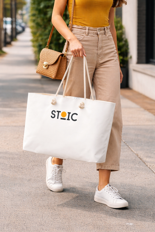 Person holding a white tote bag with 'STOIC' logo on a sidewalk.