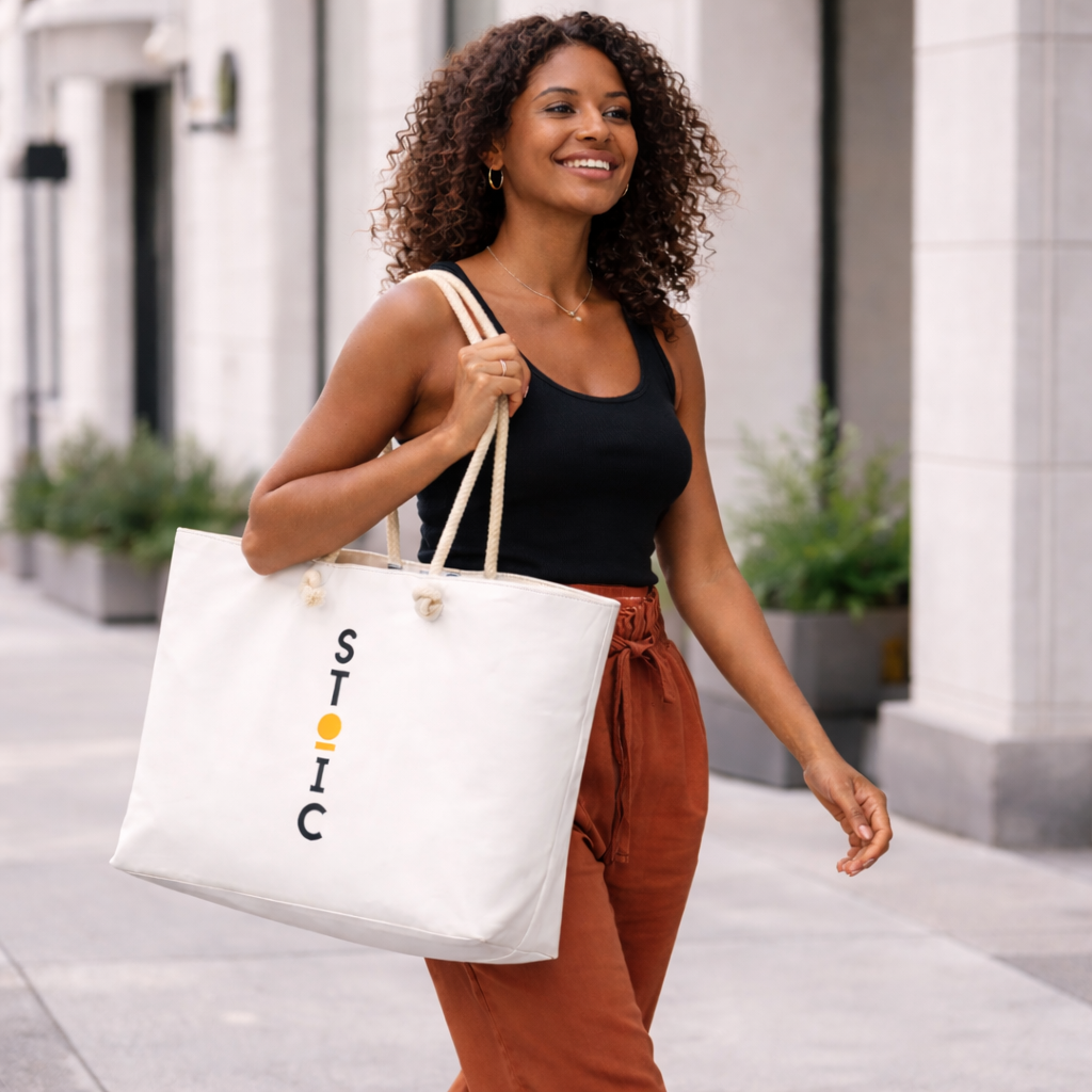 Woman holding a white STOIC tote bag with branding on a city street.