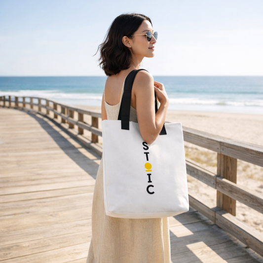 Woman holding a STOIC tote bag with text logo on a wooden boardwalk by the beach