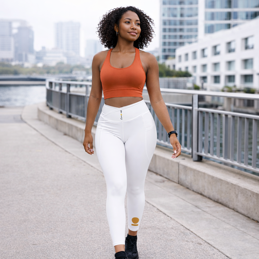 Woman in orange crop top and white STOIC leggings with logo vertical on waist and logo on front left shin, walking on a sidewalk with buildings in the background.