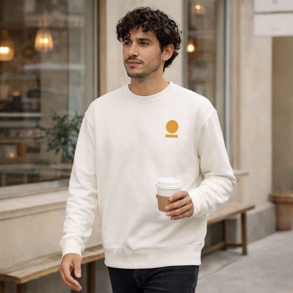 Man wearing a white STOIC sweatshirt with a embroidered logo, holding a coffee cup, in an indoor setting.