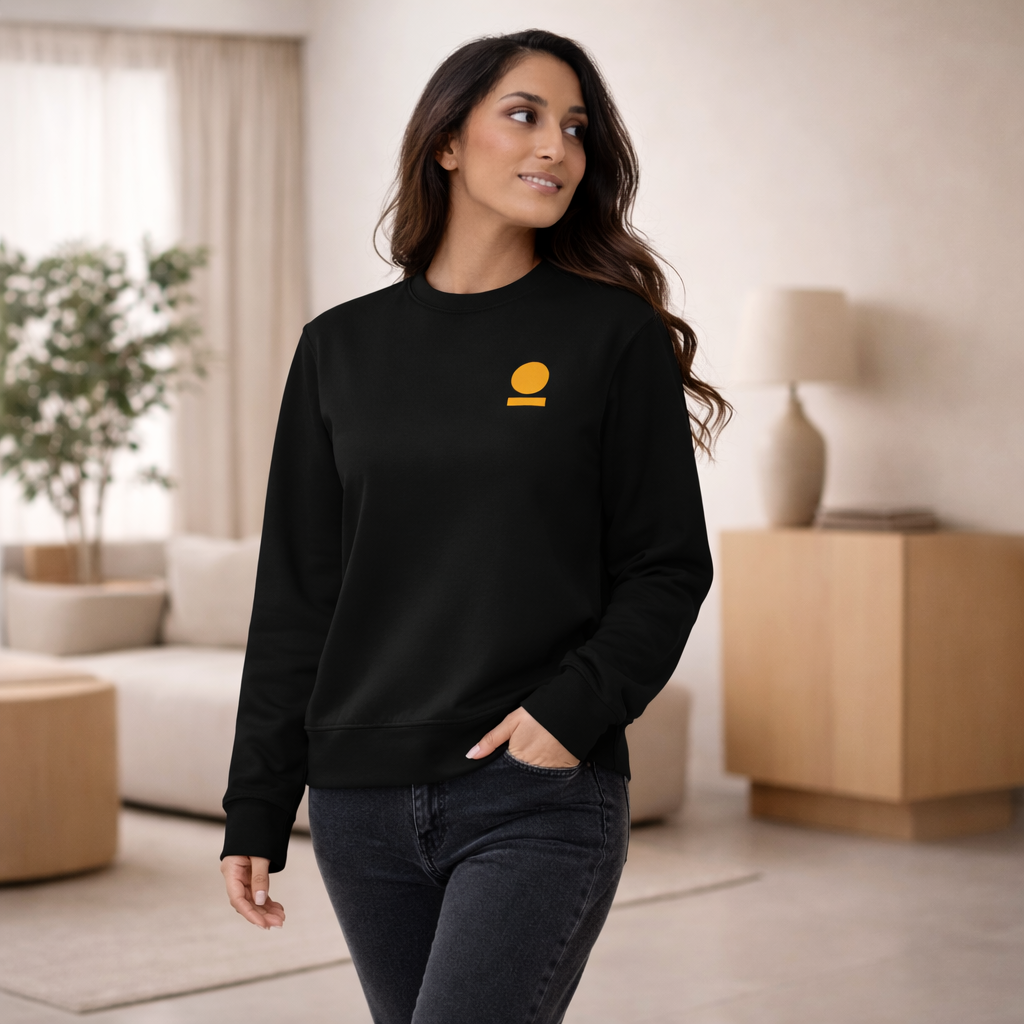 Woman wearing a black STOIC sweatshirt with embroidered logo in a living room setting