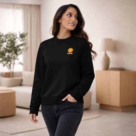Woman wearing a black STOIC sweatshirt with embroidered logo in a living room setting