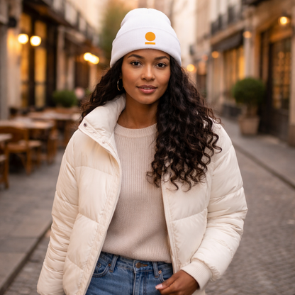 Woman wearing a white puffer jacket and STOIC beanie with embroidered logo on a city street.