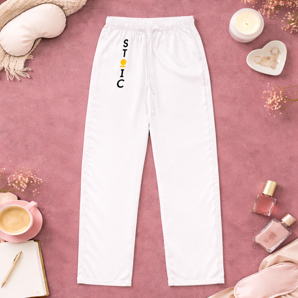 White sweatpants with vertical 'STOIC' logo on a pink surface with decorative items.