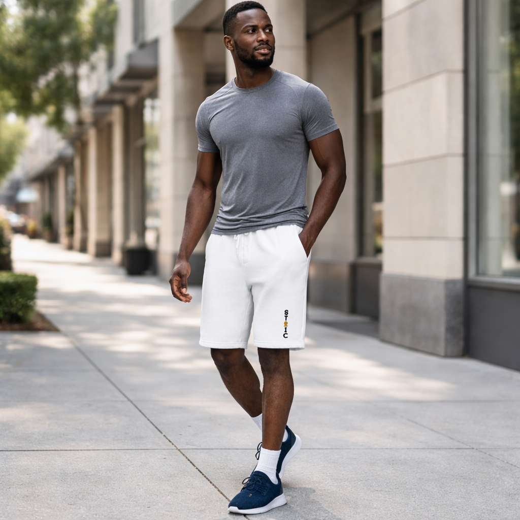 Man walking on a sidewalk wearing a gray t-shirt, white shorts with embroidered STOIC brand logo vertical, and blue sneakers.