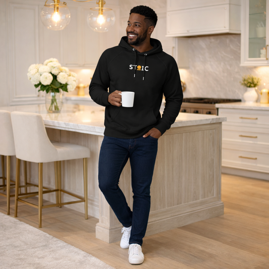 Man wearing a black STOIC hoodie with embroidered 'STOIC' logo in a kitchen holding a white mug.