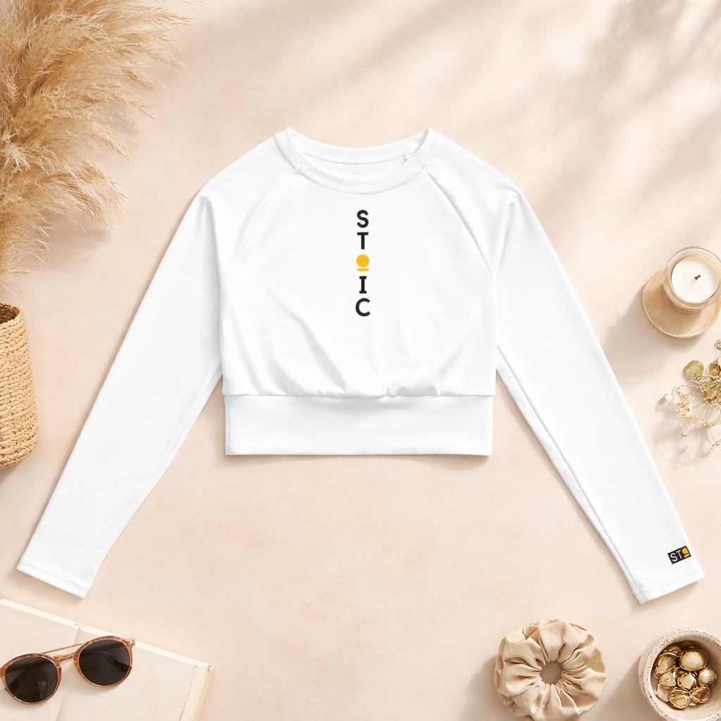 White long-sleeve crop top with 'STOIC' branding on a beige surface with decorative items.