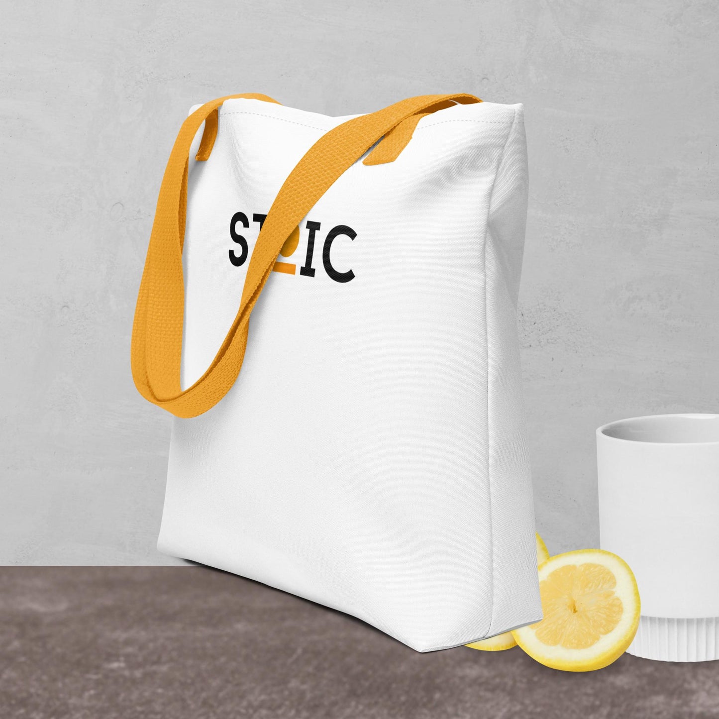 White STOIC tote bag with yellow strap and logo on a gray background