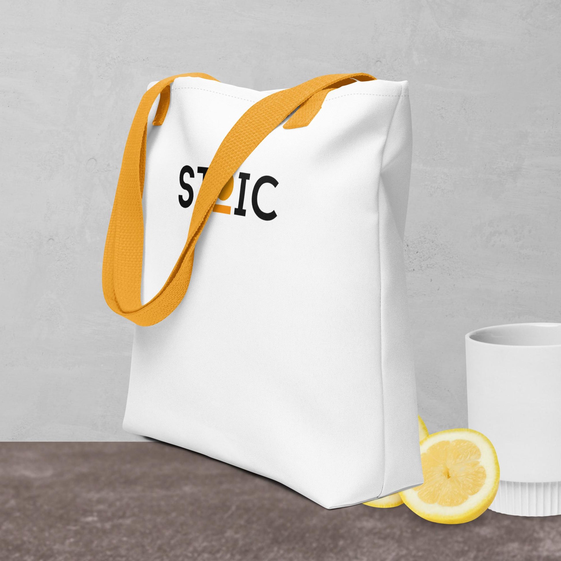 White STOIC tote bag with yellow strap and logo on a gray background