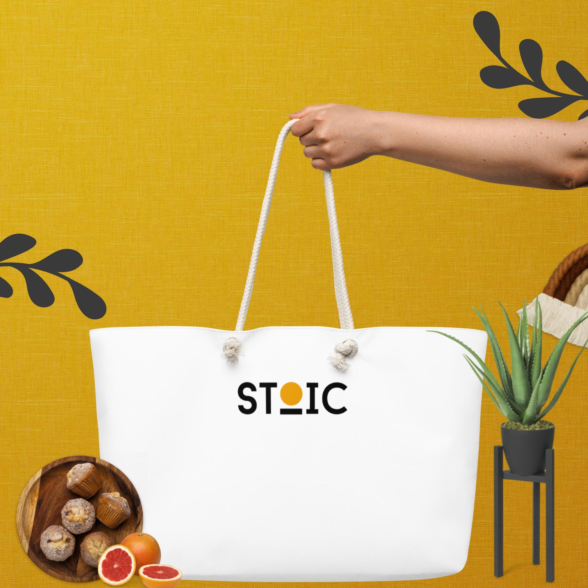 White tote bag with 'STOIC' logo held by a hand against a yellow background with decorative elements.